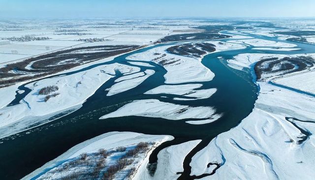 Aerial braided river carving snowy floodplain with winding sandbars and icy channels