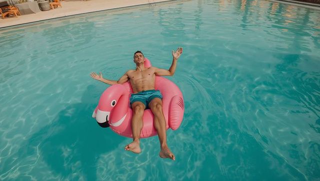 Man relaxing on pink flamingo float in resort pool under bright sunny summer sky