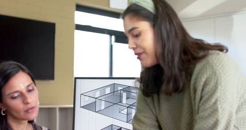 Diverse female architects reviewing floor plan on monitor in bright collaborative office