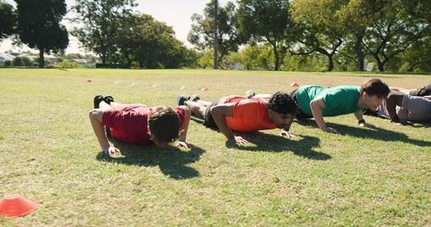 Diverse male team doing pushups in outdoor fitness drill on sunny sports field