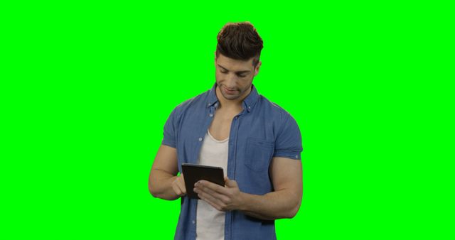 Man using digital tablet against green screen background. This image can be used for technology-related content, website banners, advertisements, or educational materials. The green screen allows for easy background replacement in editing, making it versatile for various creative projects.