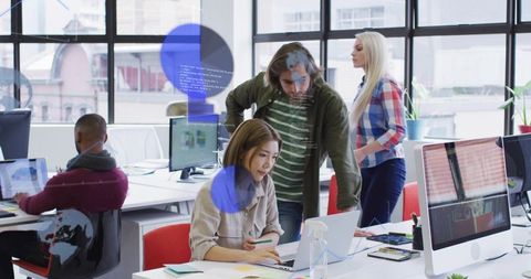 Collaborating in modern open-plan office while reviewing laptop and desktop screens