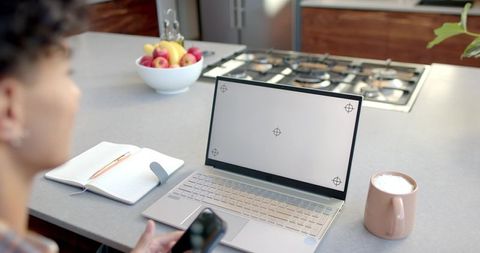 Young man working remotely at kitchen island with laptop smartphone, minimal home office