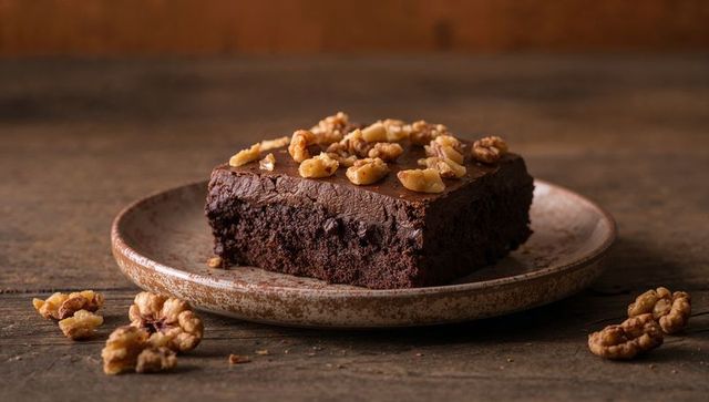 Decadent fudgy chocolate brownie topped with walnut halves on rustic ceramic plate