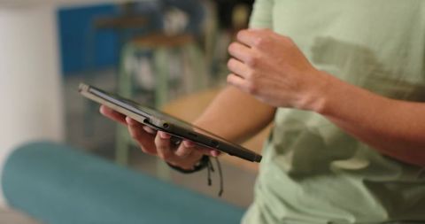 African american man holding tablet and gesturing while sitting on teal bench