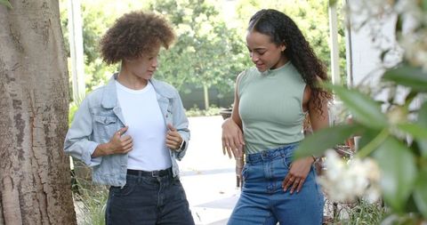 African american women chatting on shaded garden walkway in denim and casual outfits