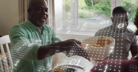 Multigenerational family passing bowl of rolls around dining table with binary data overlay