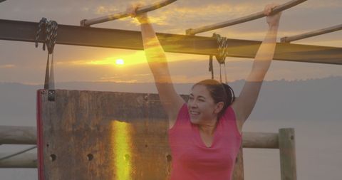 Woman hanging on obstacle course at sunset