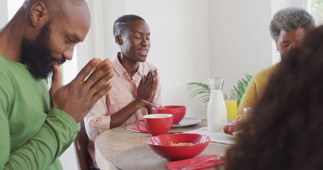 Image of happy african american parents, daughter and grandmother saying grace at dinner table. Family, domestic life and togetherness concept digitally generated image.