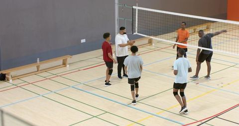 Coach leading diverse male volleyball team during indoor training and tactical drill