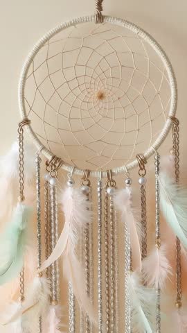 Bohemian dreamcatcher swaying with beads and feathers against soft beige wall vertical video
