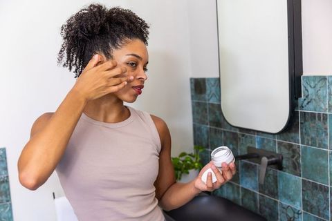 Applying facial moisturizer at bathroom mirror for daily skincare and glowing skin