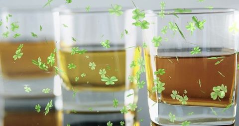 Glasses glinting with amber whiskey and floating green clover decals on reflective surface
