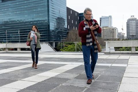 City pedestrians using smartphones and takeaway coffee while walking across tiled plaza