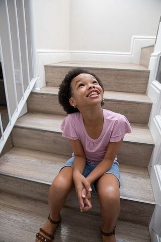 Happy Young Girl Sitting on Home Stairs Smiling Upward
