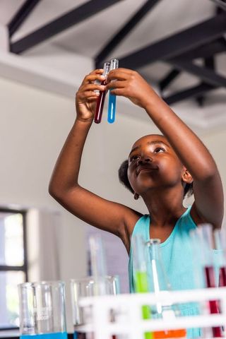African american girl conducting chemistry experiment holding red and blue test tubes