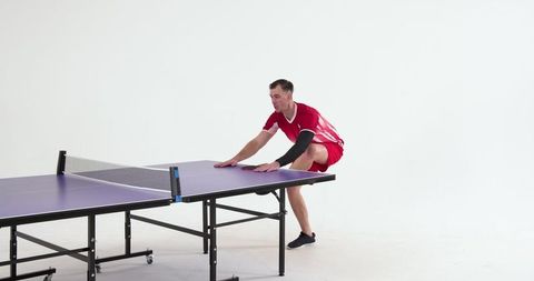 Athlete crouching beside table tennis table in studio setting