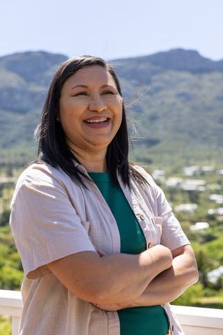 Confident mature woman smiling on balcony overlooking mountain valley, outdoor portrait