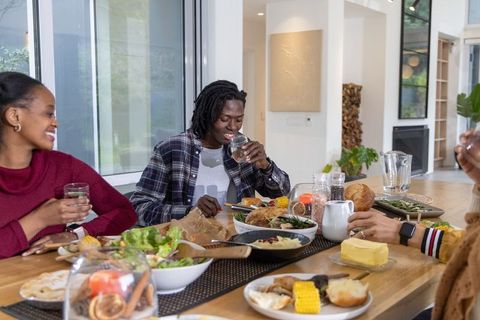 Diverse friends enjoying casual dinner around modern wooden table in open-plan home
