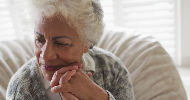 Elderly woman with grey hair sitting comfortably and gazing thoughtfully. This could be used for topics on aging, mental health, relaxation, geriatric care, and senior lifestyles. Ideal for blogs, articles, and advertisements focused on elderly well-being and contemplation.