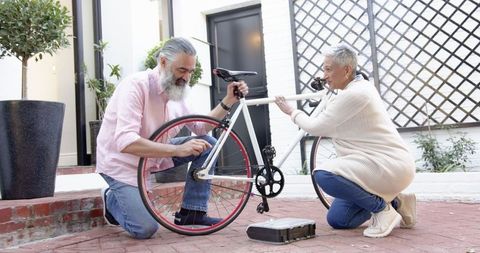 Senior couple repairing bicycle in outdoor patio collaboration