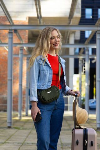 Young woman traveling with suitcase and smartphone smiling in urban plaza