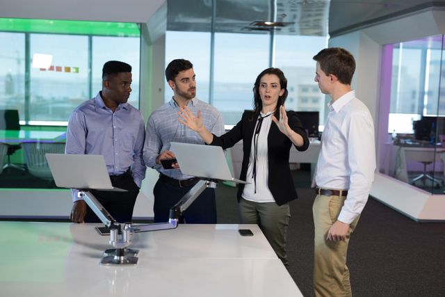 Group of executives collaborating in a modern office environment. They are engaged in a discussion around laptops, showcasing teamwork and professional interaction. Ideal for use in business presentations, corporate websites, and articles on teamwork and office dynamics.