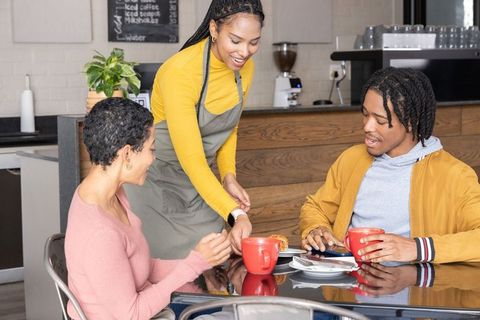 Smiling african american barista serving pastry to friends over coffee in cozy cafe