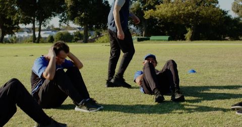 Male teammates performing sit-ups on grass during outdoor team fitness training session