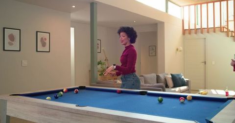Diverse women playing pool on blue-felt table in modern home lounge, woman pointing