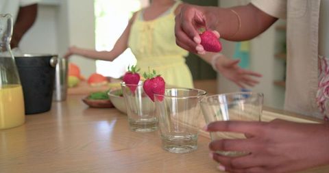 Placing fresh strawberries on glasses for sunny kitchen brunch