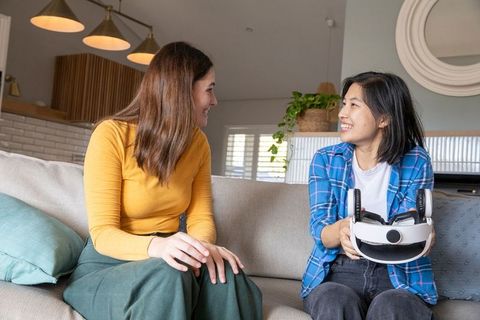 Smiling young women discussing virtual reality technology at home