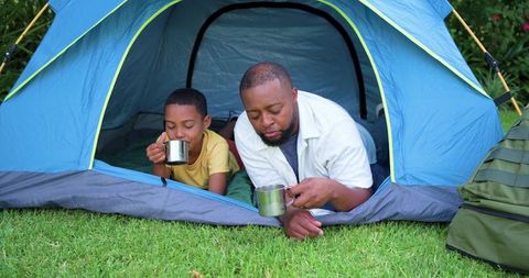 Father and son camping in backyard tent drinking from metal mugs
