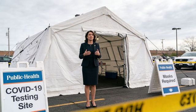 Public health official addressing community at outdoor covid-19 testing tent, masks required
