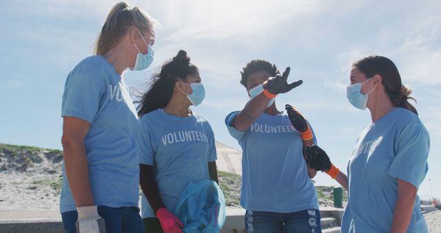 Group of volunteers cleaning a beach while wearing gloves and masks. This can be used for promoting environmental conservation, social responsibility, volunteer work, and community service initiatives.