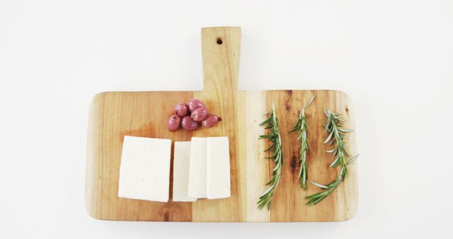 A wooden cutting board presents a simple arrangement of cheese, grapes, and rosemary sprigs, with copy space. Its minimalistic layout is ideal for themes related to food preparation or culinary presentation.