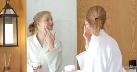 Woman Applying Moisturizer in Bathroom for Skincare Routine