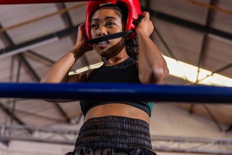 Focused african american female boxer adjusting red headgear in boxing ring