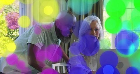 Mature couple collaborating on laptop at home with vibrant bokeh overlay and natural light