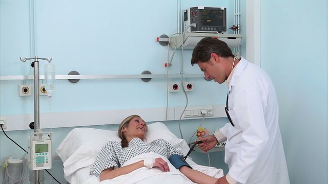 Doctor attending to a female patient in a hospital bed. The patient is smiling, suggesting a positive interaction. The doctor performs a blood pressure check, highlighting a routine medical procedure. Ideal for healthcare, doctor's visit, medical care, patient care, health check campaigns.