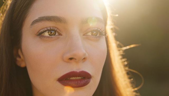 Gazing woman at golden hour with dark red lipstick, lens flare and contemplative closeup