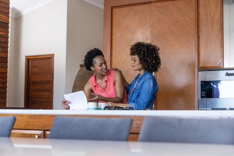 Mid-adult diverse women reviewing household bills at cozy wooden kitchen island