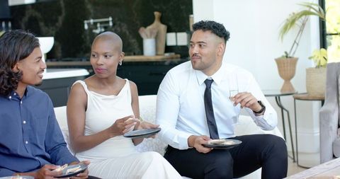 Stylish friends enjoying drinks and appetizers on sofa during elegant home cocktail party