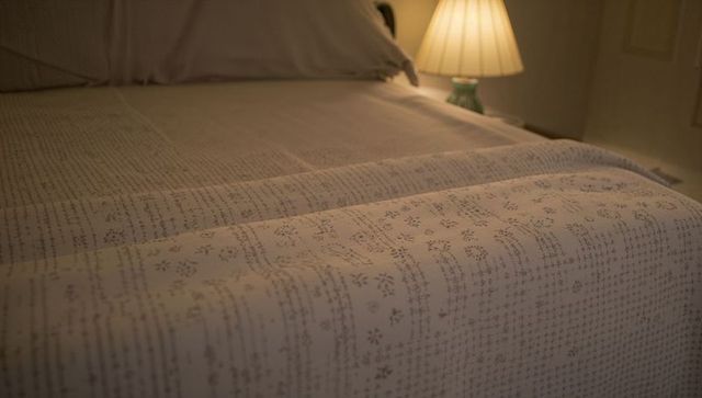 Cozy patterned coverlet draping over bed with warm lamp glow and soft pillow