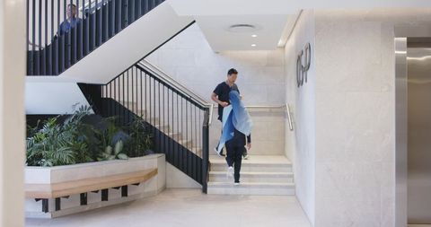 Diverse professionals walking staircase in modern atrium lobby with planter bench
