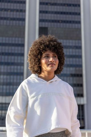 Woman standing in front of office tower wearing white hoodie looking upward urban portrait