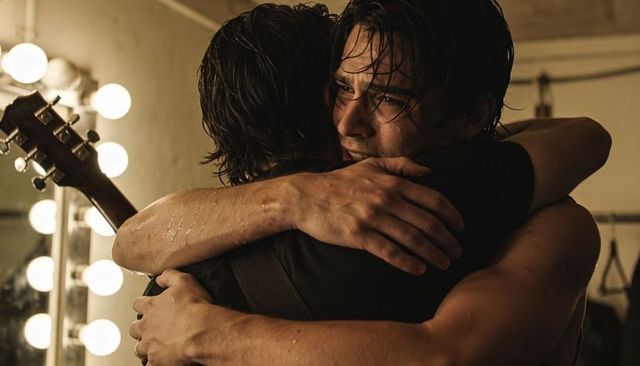 Two musicians hugging backstage at dressing room mirror after intense set, emotional triumph