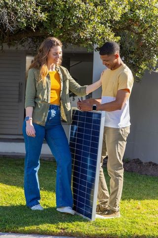 Young couple holding solar panel, collaborating on residential renewable energy upgrading
