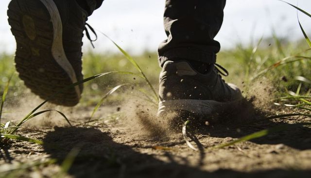 Low-angle running stride kicking up dust on dirt trail close-up of sneakers