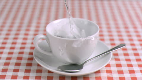Slow Motion Pouring Water into Teacup on Checkered Table